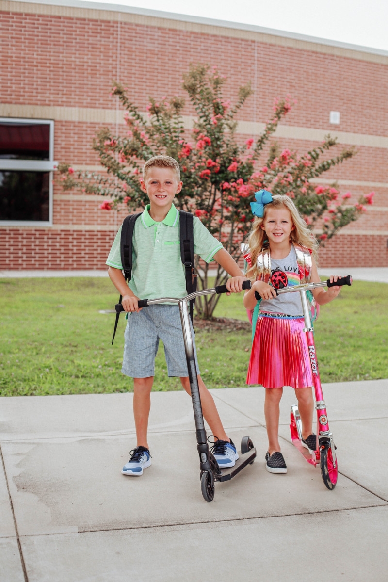 back to school | Walmart Back To School Shopping by popular Florida fashion blog, Haute and Humid: image of a boy and girl wearing Walmart back- to-school outfits and standing on their scooters in front of their elementary school. The girl is wearing a Walmart 365 Kids From Garanimals Flutter Graphic Tank Top, 65 Kids From Garanimals Shimmer Foil Pleated Skirt, and Wonder Nation Solid and Printed Bike Shorts, 2-Pack. The boy is wearing Walmart Athletic Works Boys' Slip On Cage Athletic Shoes, green Wonder Nation Short Sleeve Stretch Jersey Polo, and Wonder Nation Rib Waist Pull on Short.