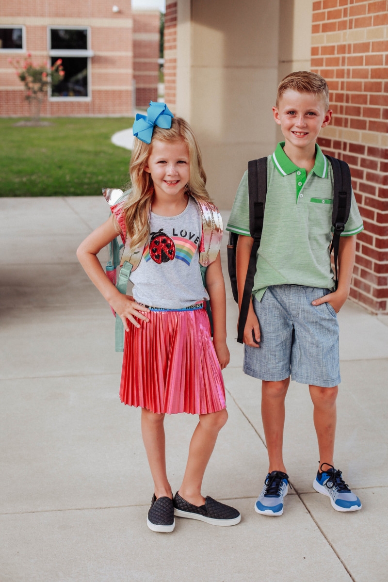 walmart back to school | Walmart Back To School Shopping by popular Florida fashion blog, Haute and Humid: image of a boy and girl standing next to each other outside of their school. The girls is wearing a Walmart 365 Kids From Garanimals Flutter Graphic Tank Top, 65 Kids From Garanimals Shimmer Foil Pleated Skirt, and Wonder Nation Solid and Printed Bike Shorts, 2-Pack. The boy is wearing Walmart Athletic Works Boys' Slip On Cage Athletic Shoes, green Wonder Nation Short Sleeve Stretch Jersey Polo, and Wonder Nation Rib Waist Pull on Short.