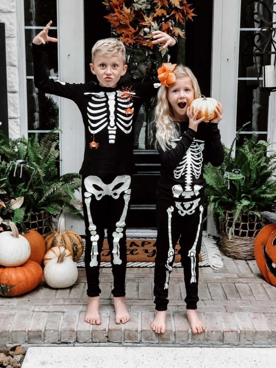 Halloween Activities | Easy Halloween Activities for Families by popular Houston lifestyle blog, Haute and Humid: image of two kids holding pumpkins on a front porch with a Target Project 62 Chevron Woven Area Rug, Etsy Happy Fall Yall Welcome Doormat, and wearing Amazon Little Pajamas skeleton glow-in-the-dark pajama sets.