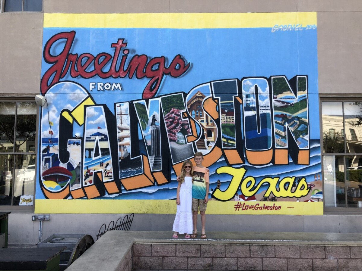 Galveston Travel Guide by popular Houston travel blog, Haute and Humid: image of two kids standing in front of a greetings from Galveston Texas sign. 
