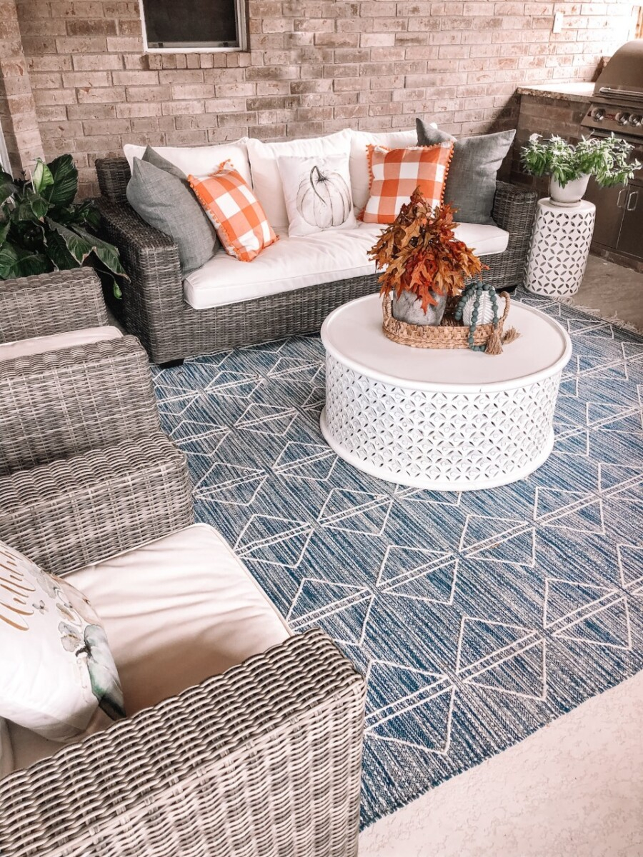 fall patio | Fall Decor by popular Houston life and style blog, Haute and Humid: image of a back patio decorated with a Pottery Barn Torrey All-Weather Wicker Square Arm 86" Sofa, Pottery Barn Torrey All-Weather Wicker Square Arm Swivel Lounge Chair, West Elm Reflected Diamonds Indoor/Outdoor Rug, Wayfair Lorraine Solid Wood Drum Coffee Table, Amazon MIULEE Set of 2 Retro Farmhouse Buffalo Plaid Check Pillow Cases, Amazon PSDWETS Autumn Decorations Pumpkin Pillow Covers, and Etsy Trellis Grey (Dark) Wooden Bead Garland. 