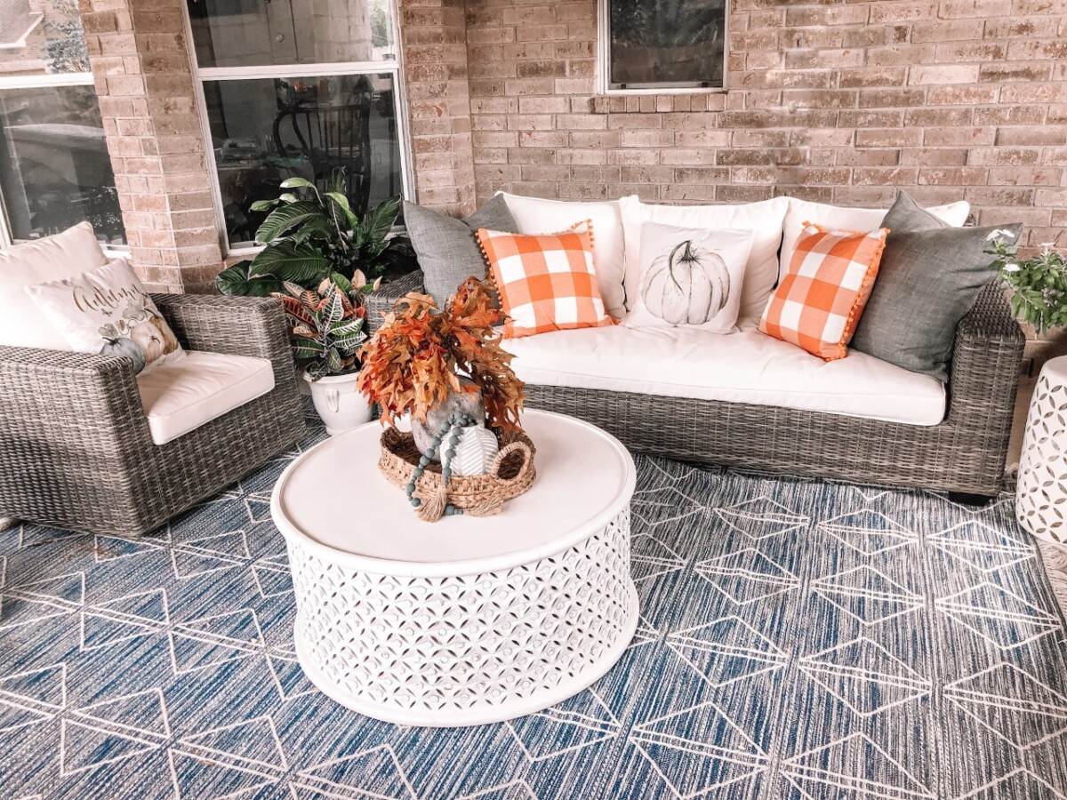 fall patio decor | Fall Decor by popular Houston life and style blog, Haute and Humid: image of a back patio decorated with a Pottery Barn Torrey All-Weather Wicker Square Arm 86" Sofa, Pottery Barn Torrey All-Weather Wicker Square Arm Swivel Lounge Chair, West Elm Reflected Diamonds Indoor/Outdoor Rug, Wayfair Lorraine Solid Wood Drum Coffee Table, Amazon MIULEE Set of 2 Retro Farmhouse Buffalo Plaid Check Pillow Cases, Amazon PSDWETS Autumn Decorations Pumpkin Pillow Covers, and Etsy Trellis Grey (Dark) Wooden Bead Garland. 