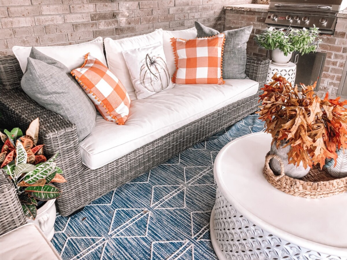 bargain fall decor | Fall Decor by popular Houston life and style blog, Haute and Humid: image of a back patio decorated with a Pottery Barn Torrey All-Weather Wicker Square Arm 86" Sofa, Pottery Barn Torrey All-Weather Wicker Square Arm Swivel Lounge Chair, West Elm Reflected Diamonds Indoor/Outdoor Rug, Wayfair Lorraine Solid Wood Drum Coffee Table, Amazon MIULEE Set of 2 Retro Farmhouse Buffalo Plaid Check Pillow Cases, Amazon PSDWETS Autumn Decorations Pumpkin Pillow Covers, and Etsy Trellis Grey (Dark) Wooden Bead Garland. 