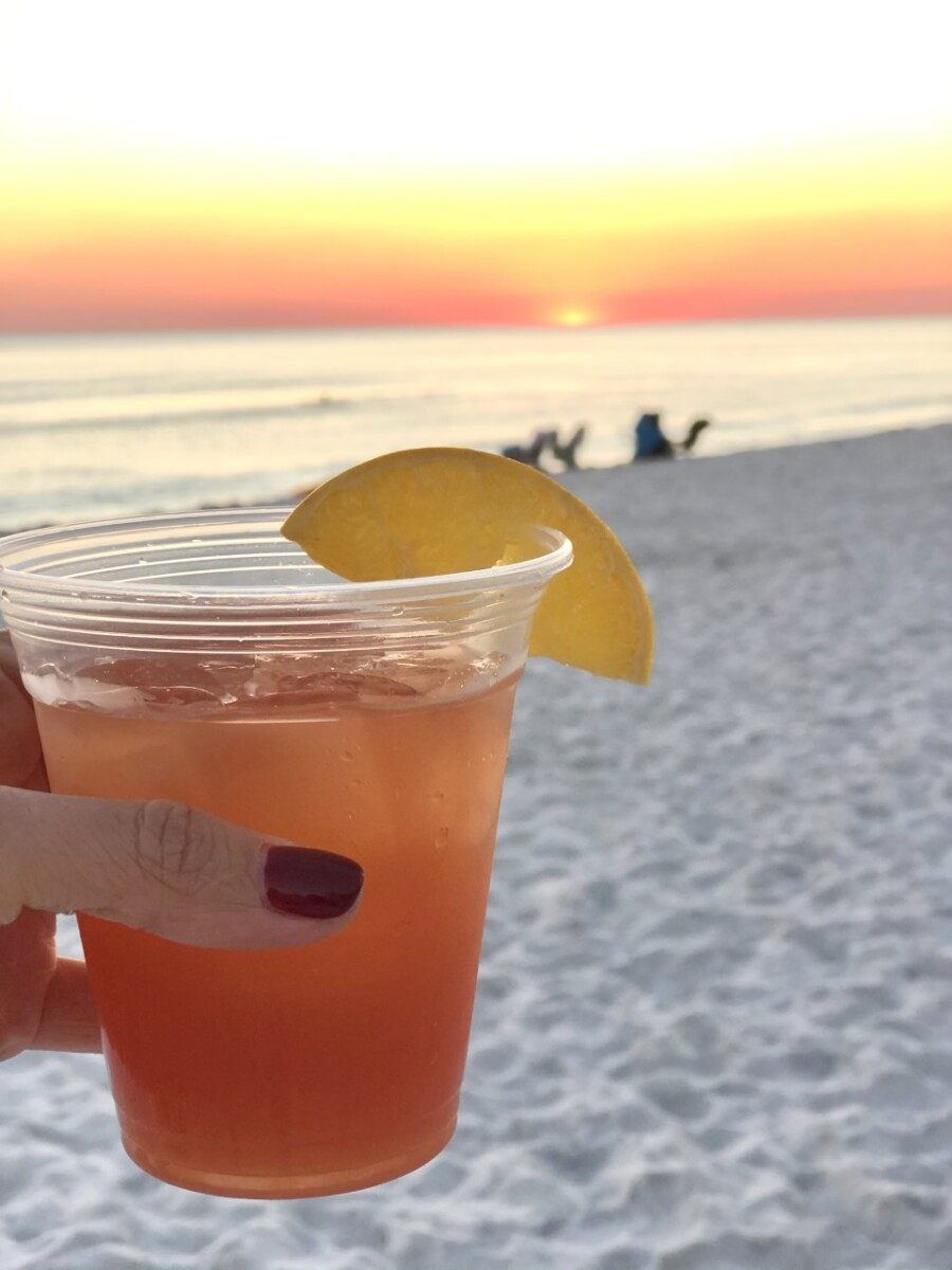 destin beach house rentals |Florida Beach House Rental by popular Houston travel blog, Haute and Humid: image of a woman holding a cocktail in her hand while on a white sand beach and watching a sunset. 