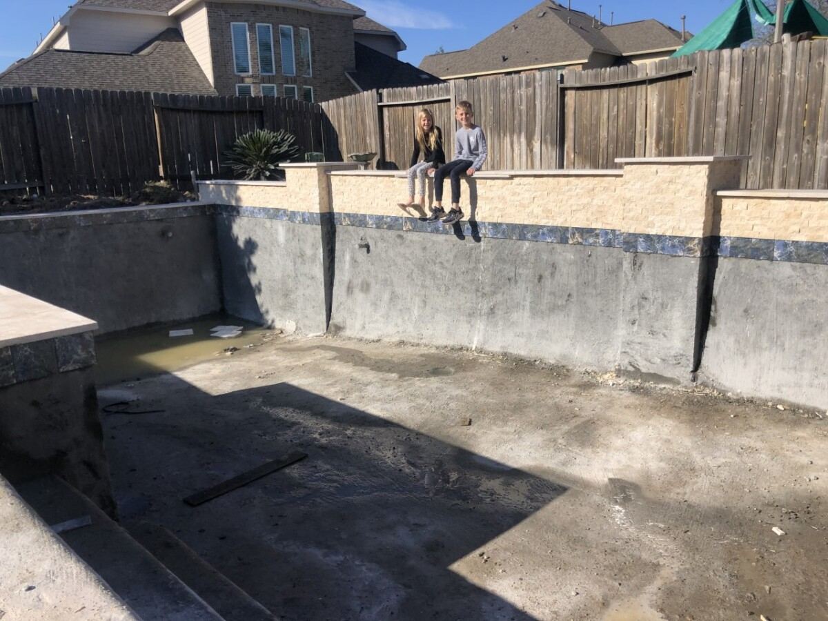 pool build | pool dig | pool before and after | Outdoor Kitchen by popular Houston life and style blog, Haute and Humid: image of two kids sitting on the edge of an unfinished pool. 