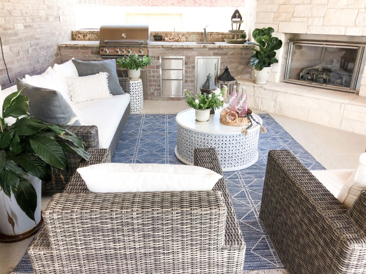 outdoor living area | Outdoor Kitchen by popular Houston life and style blog, Haute and Humid: image of a wicker patio set with white cushions, blue and white area rug, round white coffee table, and outdoor plants. 