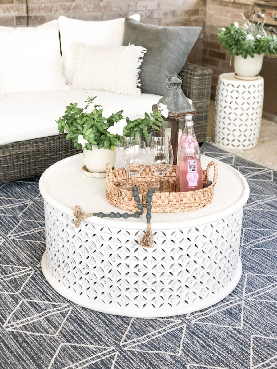 coffee table | Outdoor Kitchen by popular Houston life and style blog, Haute and Humid: image of a wicker patio set with white cushions, blue and white area rug, round white coffee table, and outdoor plants. 