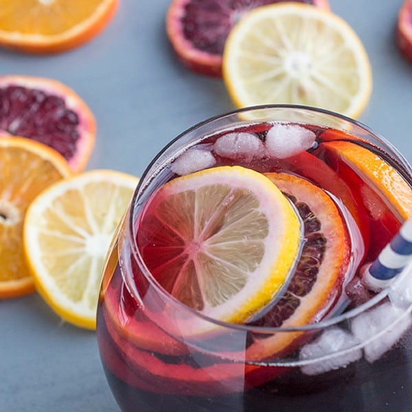 sangria | Pitcher Cocktails by popular Houston lifestyle blog, Haute and Humid: image of a sangria drink in a clear glass cup with a blue and white stripe straw. 