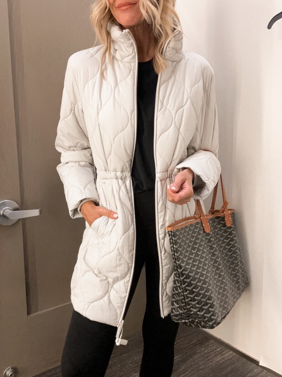 Woman wearing a white quilted jacket over a black outfit with a gray designer tote bag from the Nordstrom Anniversary Sale.